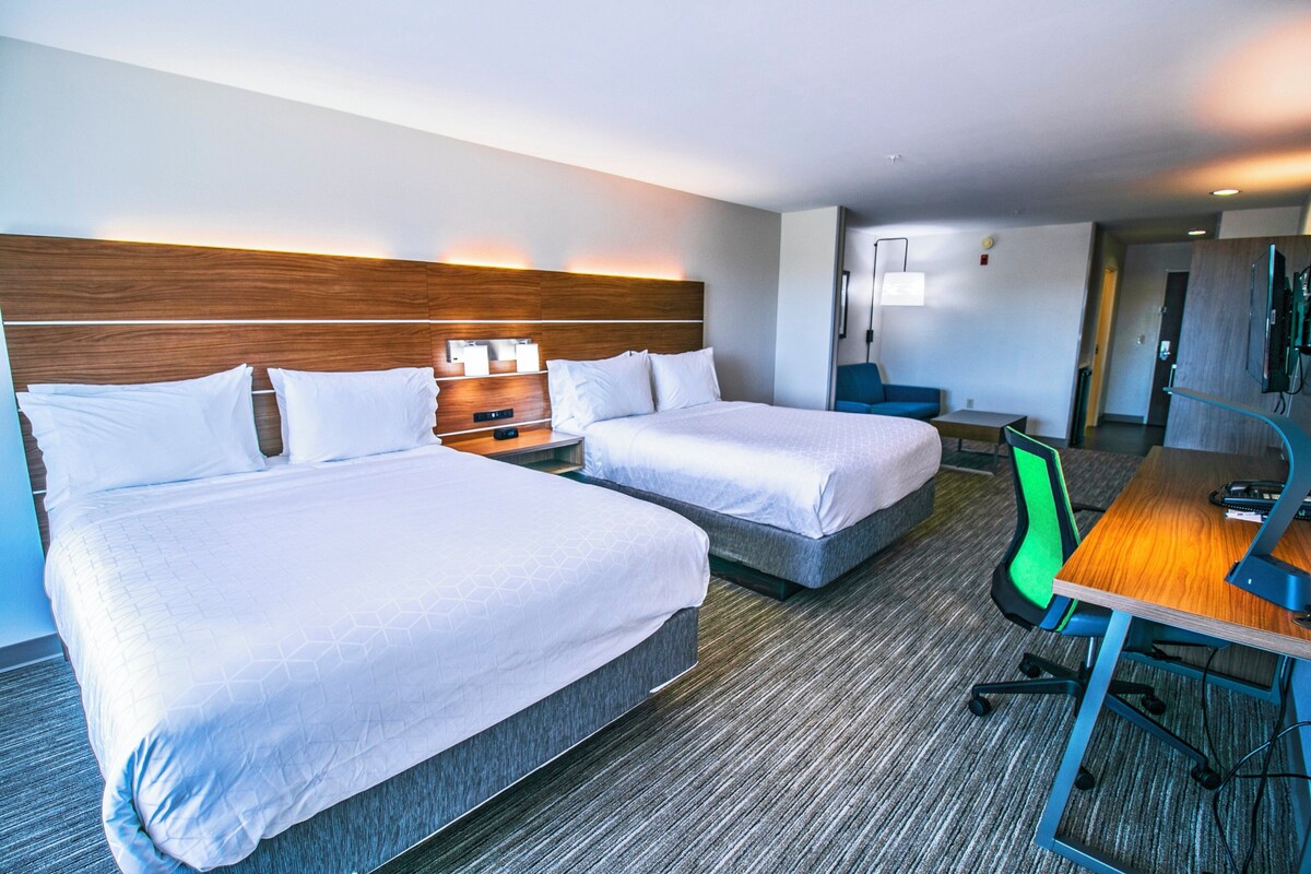 A hotel room with two beds, a desk, a chair, and a TV.