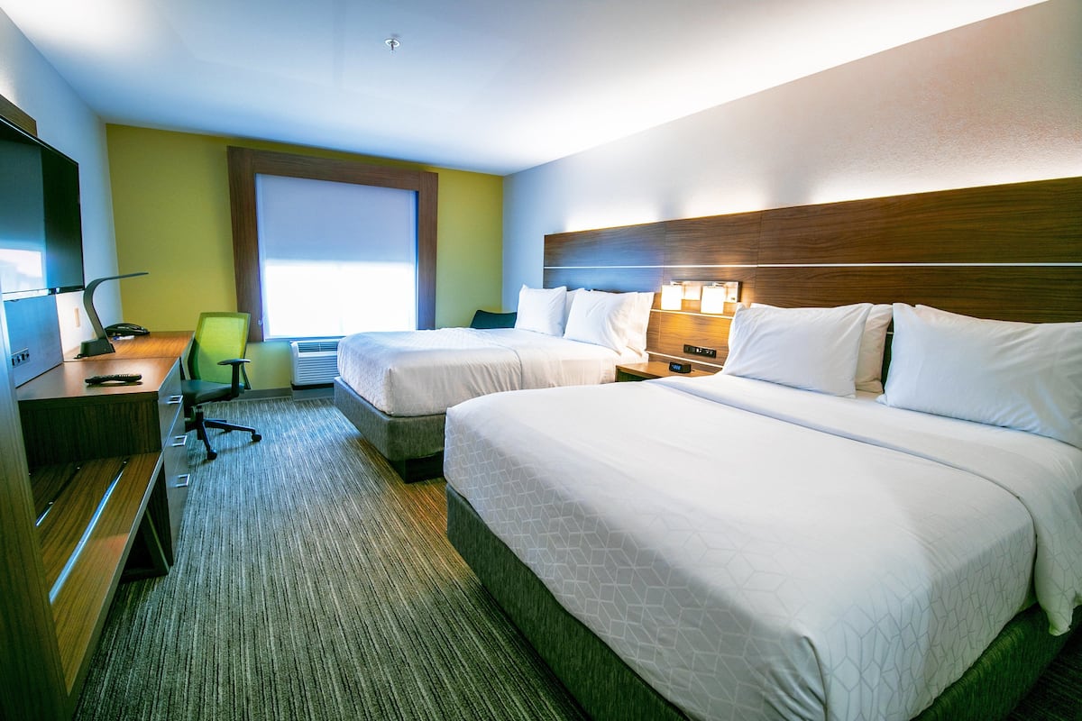 Une chambre d’hôtel avec deux lits, un bureau avec une chaise, une télévision et une fenêtre avec des stores.