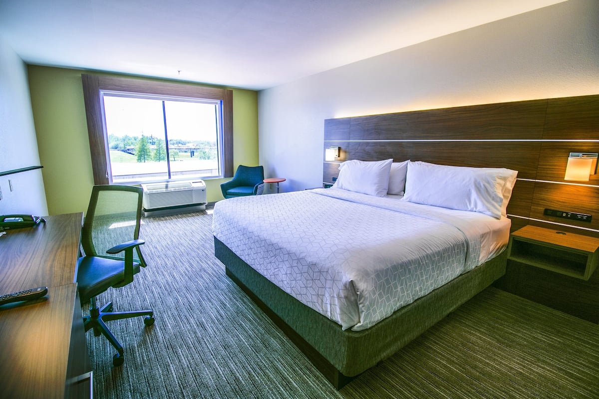 Une chambre d’hôtel avec un grand lit, un bureau avec une chaise, une petite table et une fenêtre donnant sur un beau paysage.