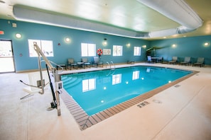 Una piscina interior con un puesto de salvavidas, una escalera de piscina y varias sillas de descanso alrededor del área de la piscina.