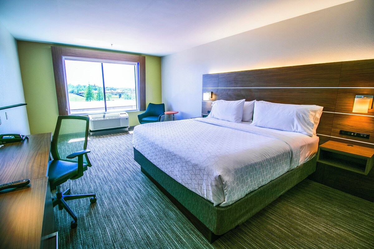 A hotel room with a large bed, a desk with a chair, a small table, and a window with a view.