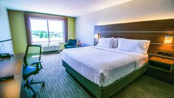 A hotel room with a large bed, a desk with a chair, a small table, and a window with a view.