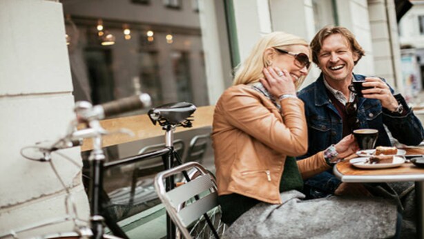Two people sitting at an outdoor cafe with a bicycle and a table with a cup and a pastry. - Holiday Inn Express & Suites Sealy by IHG (Sealy)