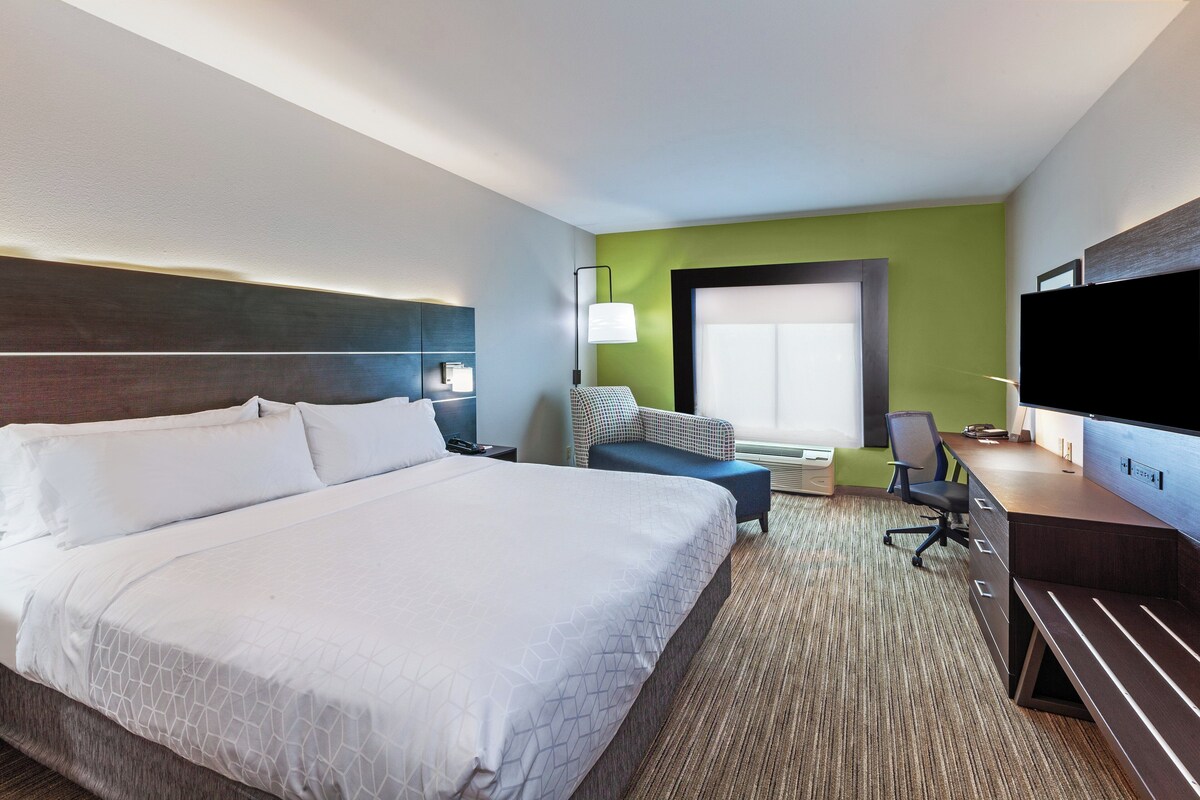 A hotel room with a large bed, a desk, a chair, a TV, and a window.