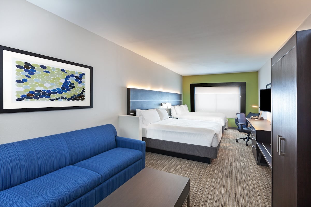 A hotel room with a bed, a blue sofa, a desk, and a television.