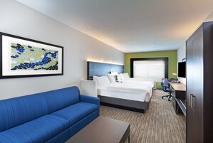 Una habitación de hotel con cama, sofá azul, escritorio y televisor.