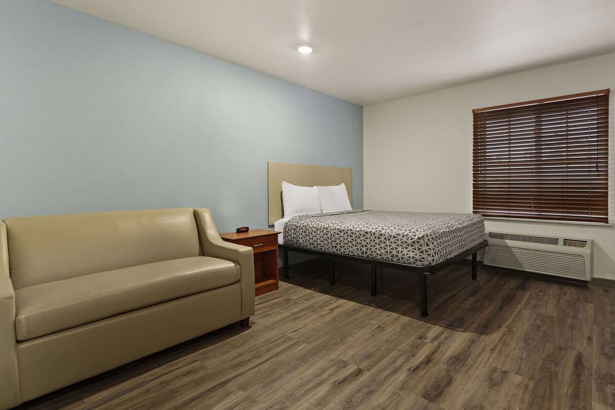 Ein Schlafzimmer mit Bett, Sofa, Nachttisch und einem Fenster mit Jalousien.