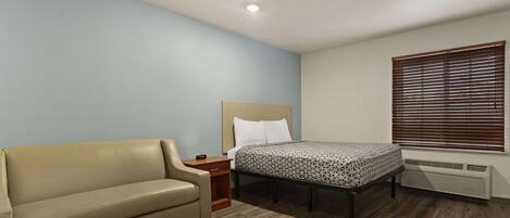 Une chambre à coucher comprenant un lit, un canapé, une table de chevet et une fenêtre avec des stores.