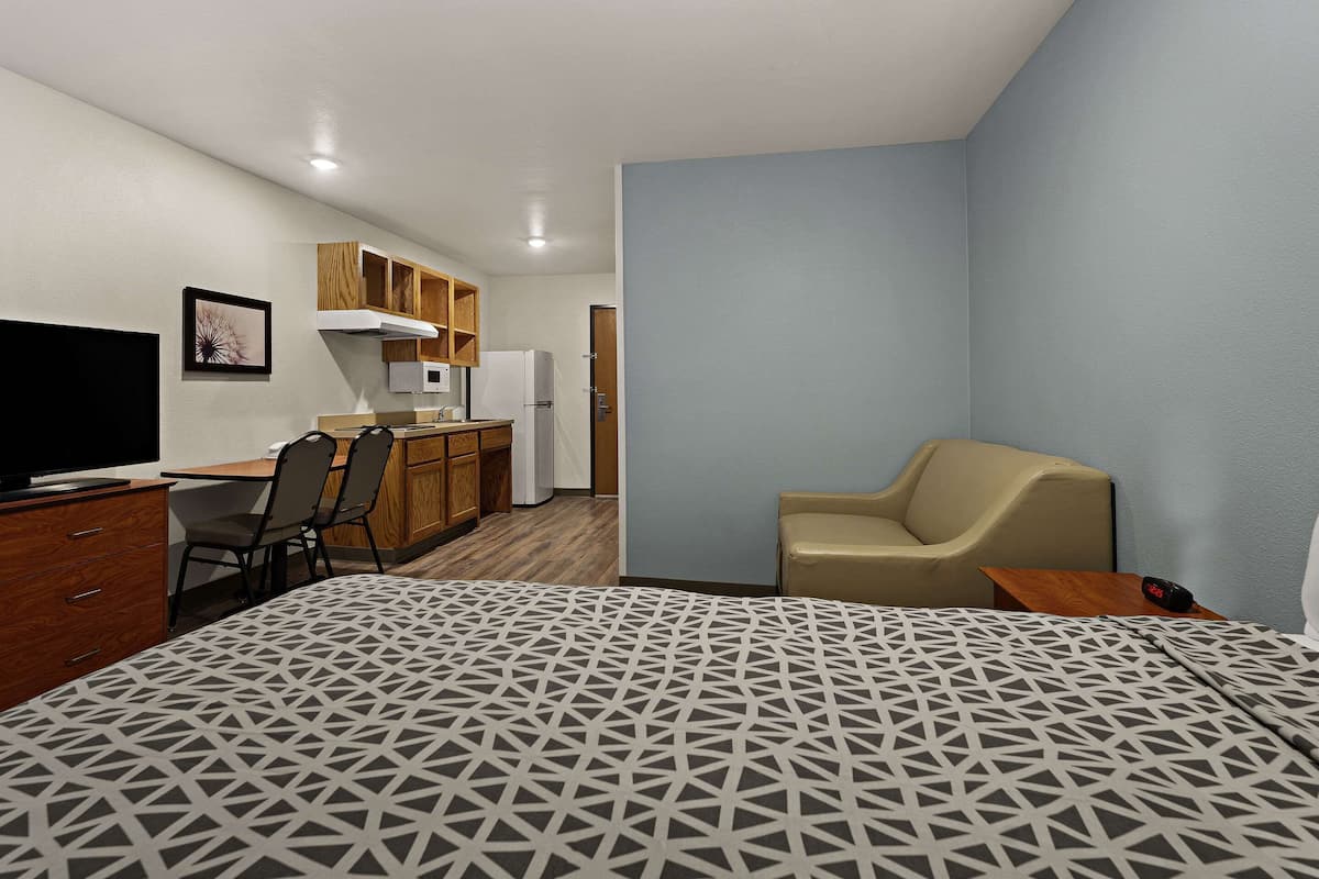 Ein kleines Hotelzimmer mit Bett, Schreibtisch mit Stuhl, einer Küchenzeile und einem Fernseher.