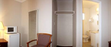 Habitación pequeña con una silla, microondas y un refrigerador compacto. Se ve un baño por un vano abierto.