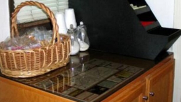 A room with a wooden cabinet, a black stove, a basket, and a window with blinds. - Sunset Inn and Suites (West Sacramento)