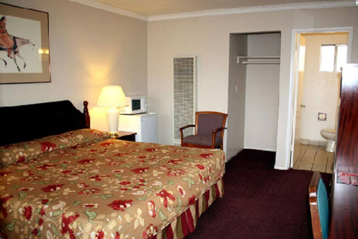 A hotel room with a large bed, a chair, a desk with a lamp, a microwave, and a door leading to a bathroom.