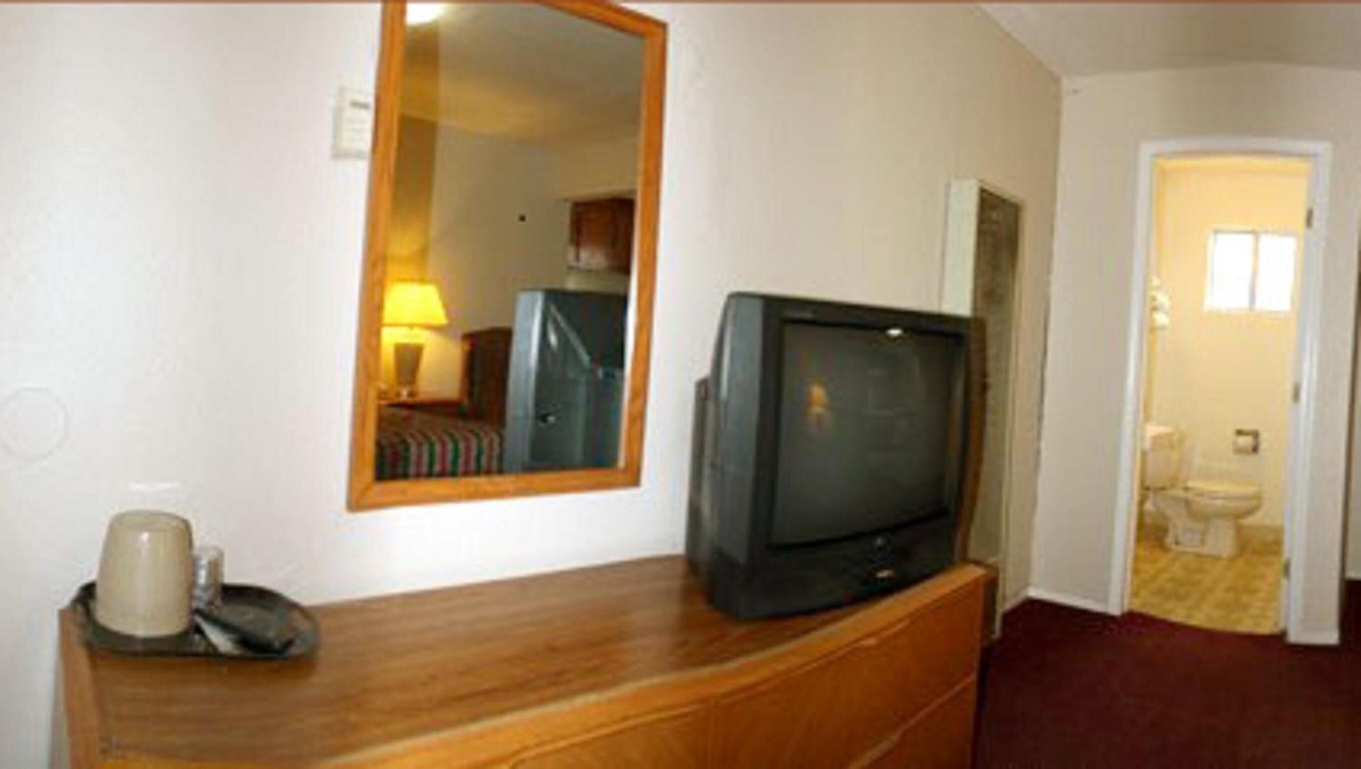 A hotel room with a wooden dresser, a television, a mirror, and a view of the bathroom.