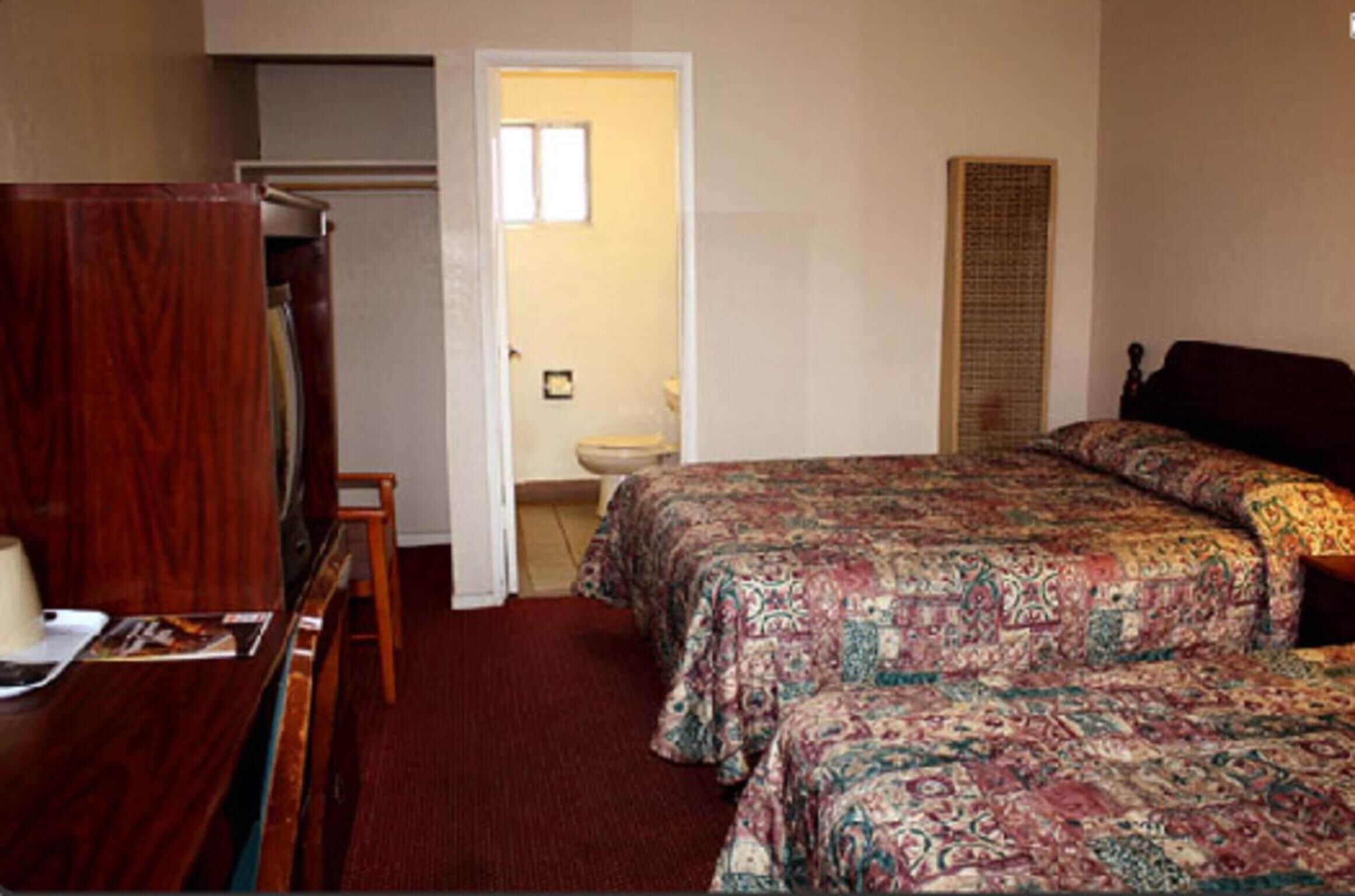 Ein Schlafzimmer mit zwei Betten, einem Holztisch, einem Stuhl, einem Kleiderschrank und einem durchgegangenen Tür erkennbaren Badezimmer.