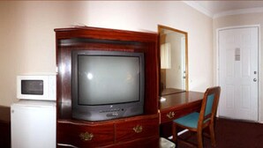 A hotel room with a wooden dresser, a television, a microwave, and a chair. - Sunset Inn and Suites (West Sacramento)