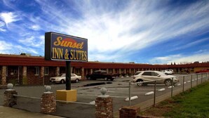 A Sunset Inn & Suites with a brick facade, a parking lot, and a clear blue sky. - Sunset Inn and Suites (West Sacramento)