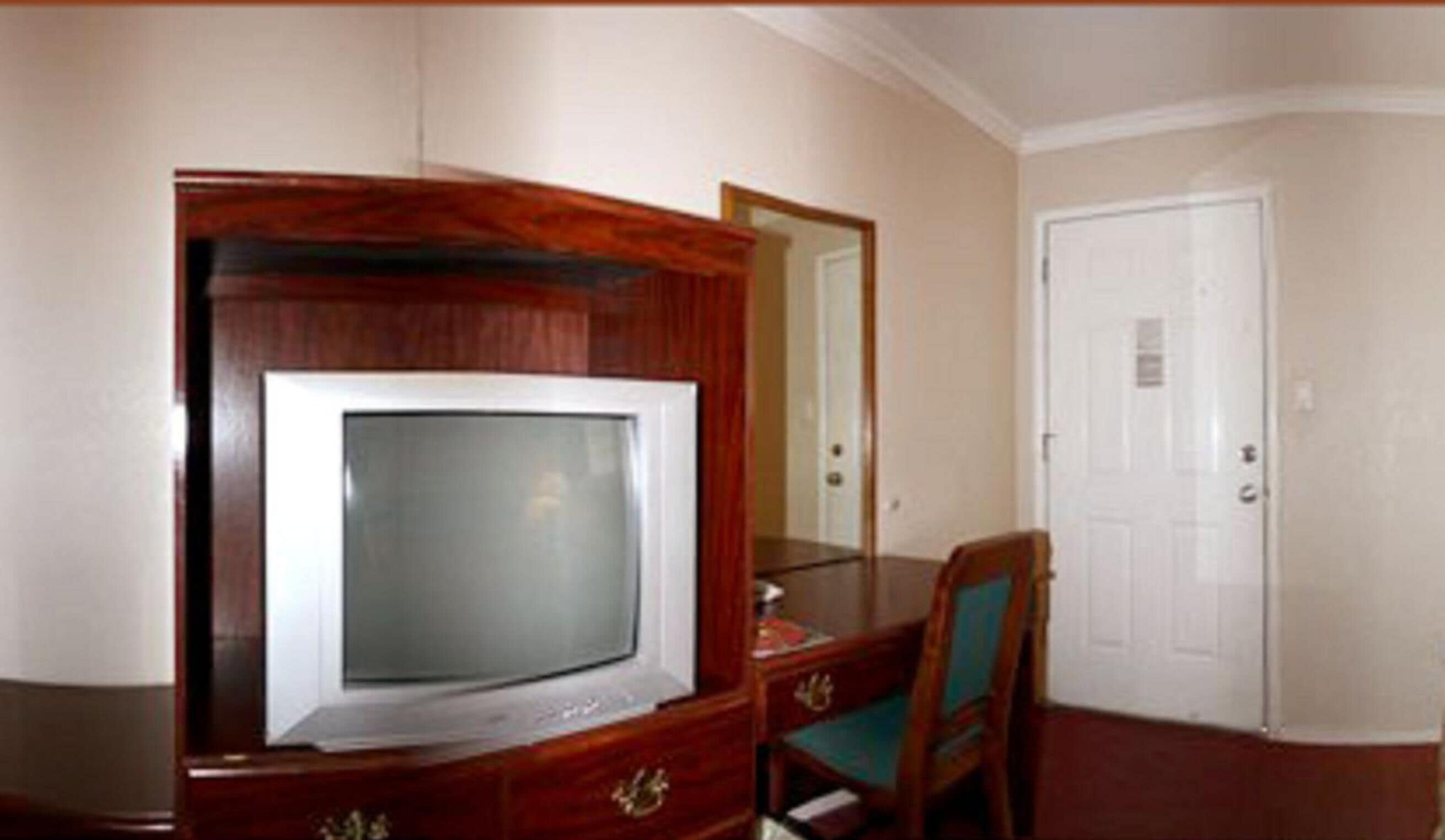 A room with a wooden desk, a television, a chair, and a door.