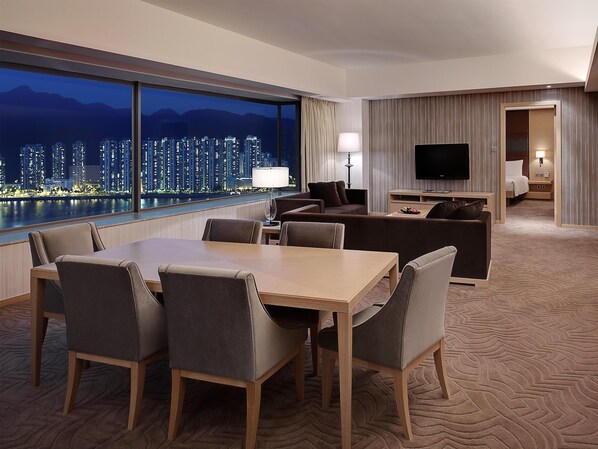 A hotel room with a dining area, a sofa, a TV, and a view of a cityscape at night. - Hyatt Regency Hong Kong, Sha Tin (Sha Tin)