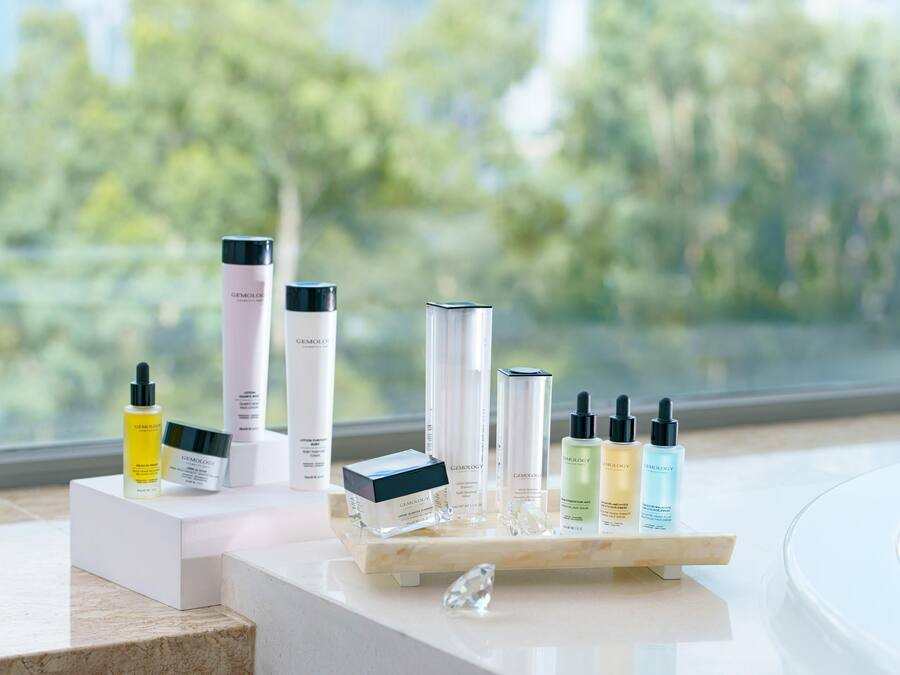A display of skincare products on a marble countertop with a view of trees through a window.