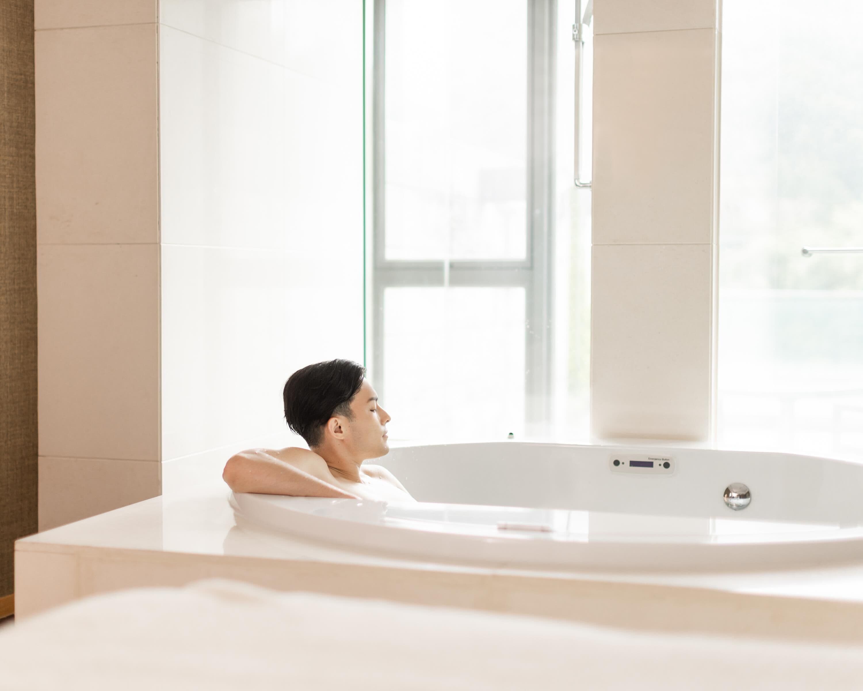Una persona si rilassa in una vasca da bagno moderna con una finestra sullo sfondo.
