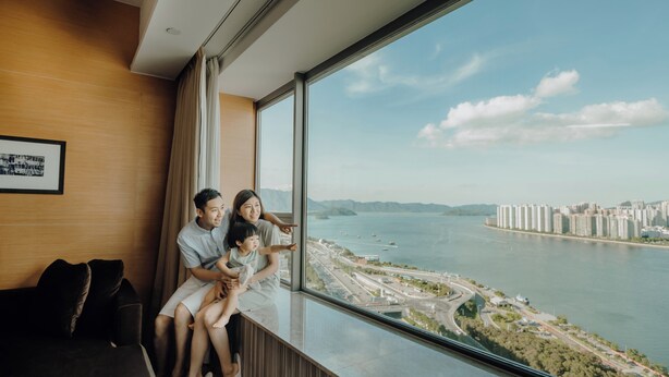 A couple sitting by a large window overlooking a river and cityscape.