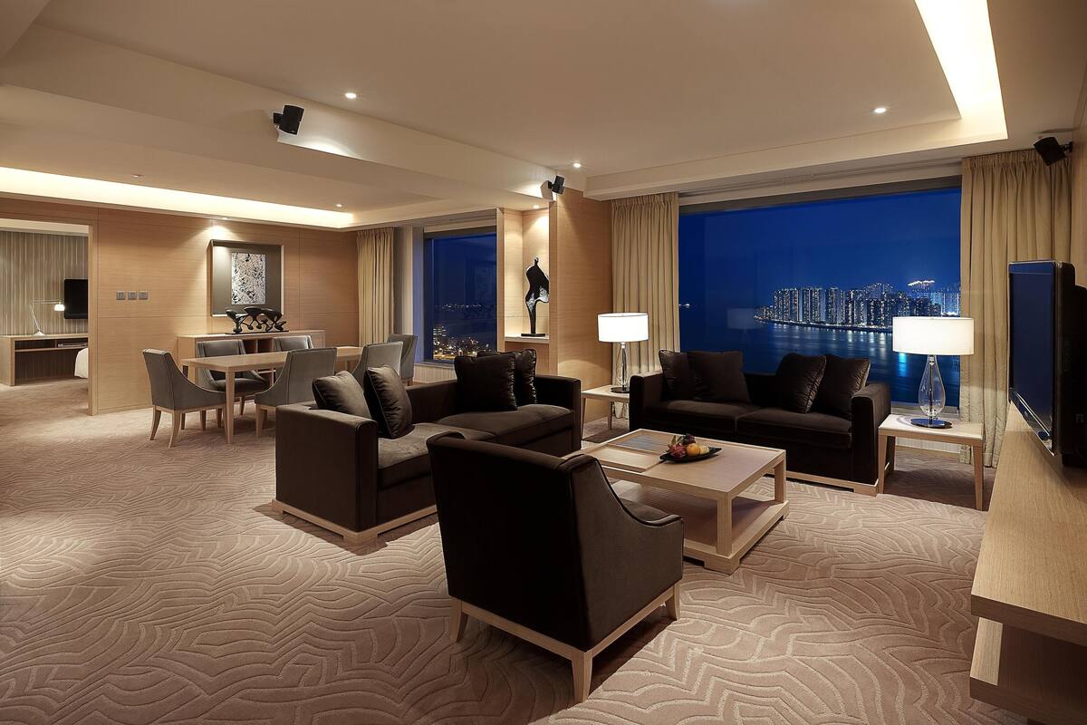 A modern hotel room with a city view, a dining area, and a seating area with sofas and a coffee table.