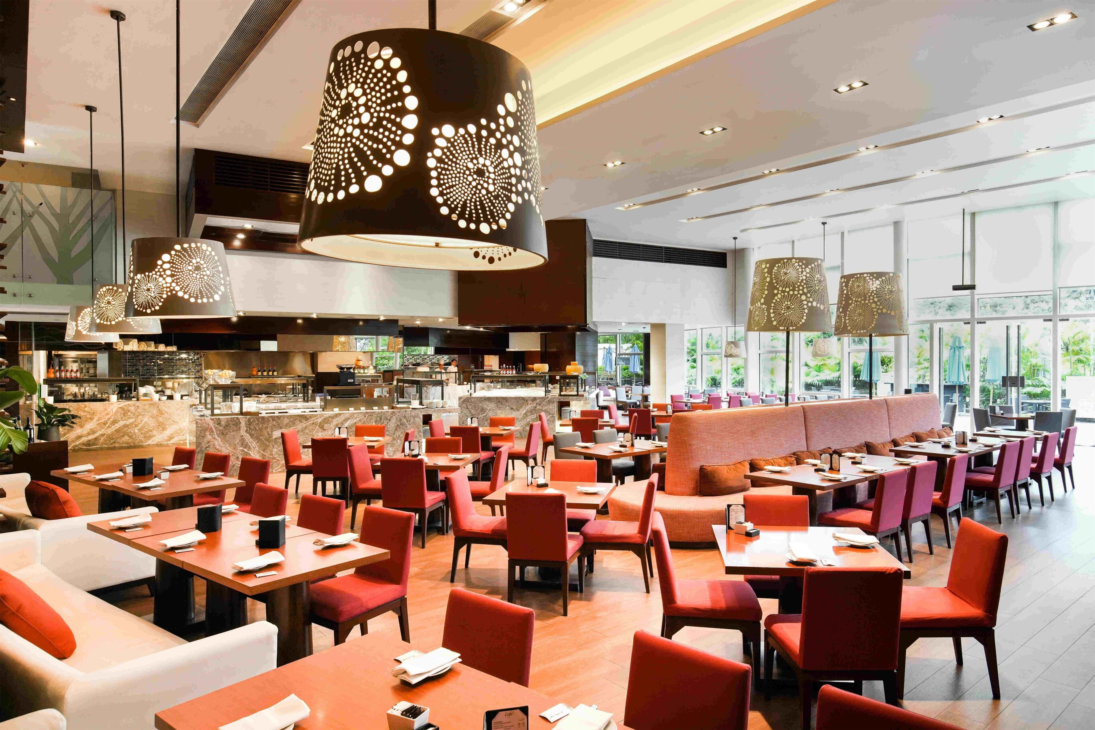 A spacious dining area with multiple tables and chairs, a central bar, and large windows allowing natural light.