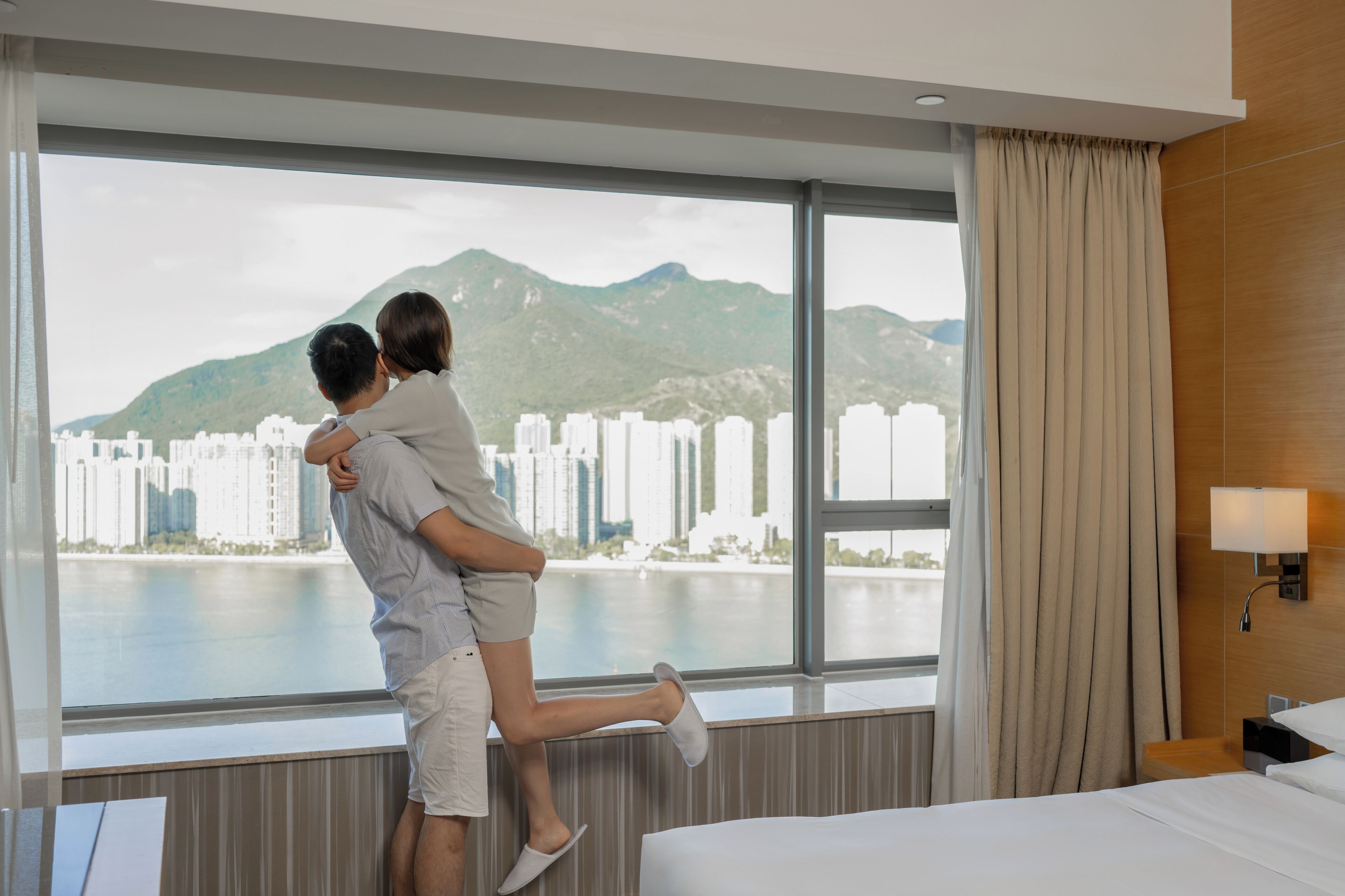 A hotel room with a large window offering a view of a cityscape and mountains.