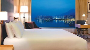 A hotel room with a large bed, a desk with a chair, and a view of a cityscape at night.
