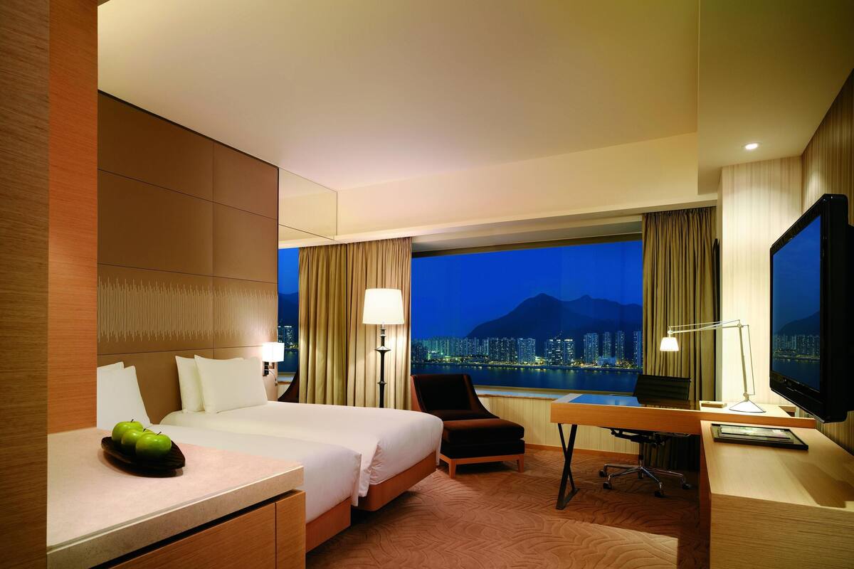 A hotel room with a bed, desk, chair, television, and a view of a cityscape at night.