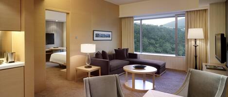 Habitación de hotel con sofá, una mesa de comedor con manzanas, televisión y un ventanal con vista al bosque.