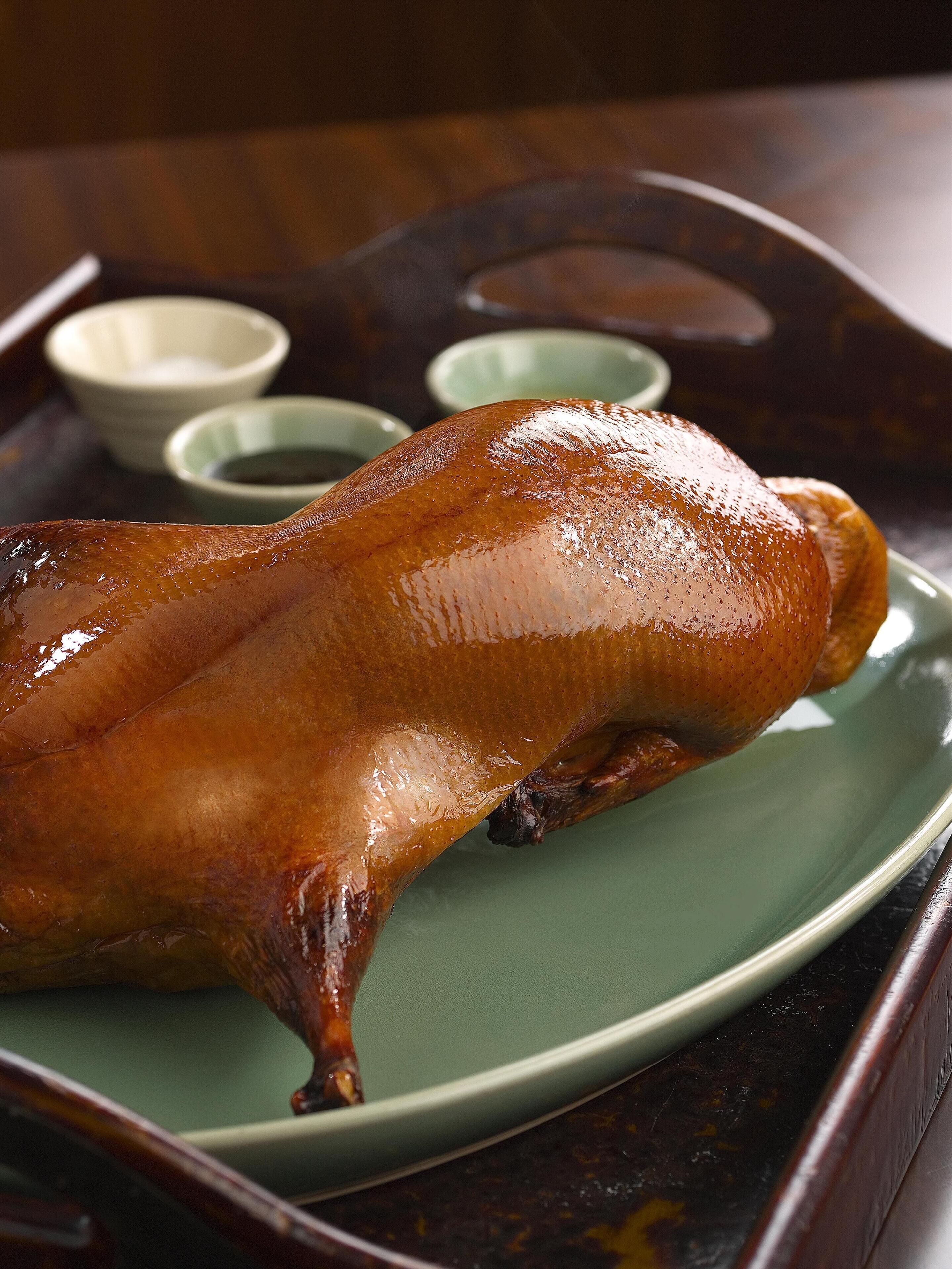 A roasted duck on a green plate with a wooden tray.