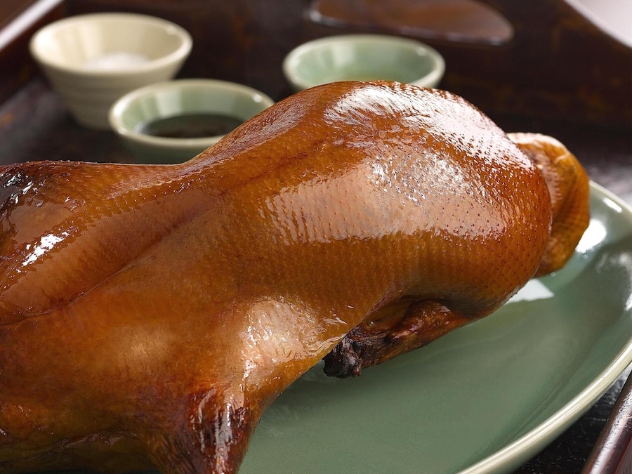 A roasted duck on a green plate with a wooden tray.