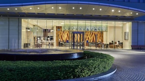 A modern hotel entrance with a glass facade, a reception desk, and a seating area visible through the glass.