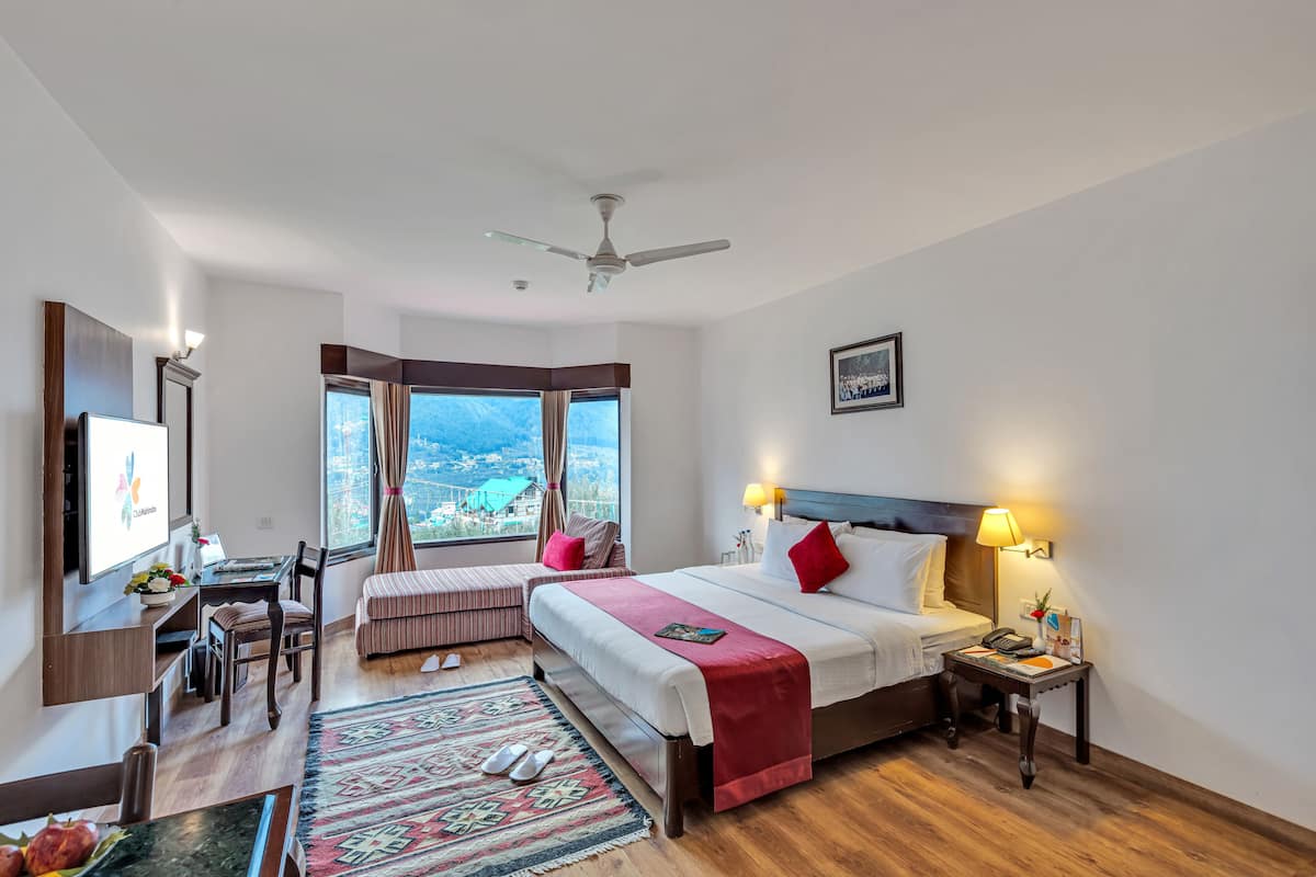 A hotel room with a large bed, a desk, a chair, a television, and a view of the city.