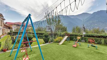 Enjoy a safe and welcoming outdoor space with swings, a slide, and exercise equipment surrounded by lush greenery and a scenic mountain view.