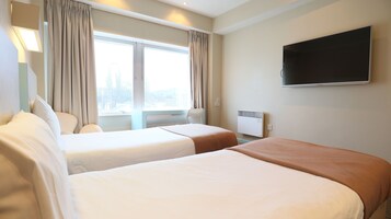 A hotel room with two beds, a TV, a window with curtains, and a radiator.