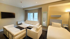 A hotel room with a sofa, two armchairs, a bed, a flat-screen TV, a mirror, and a window with curtains. - Citrus Hotel Cheltenham by Compass Hospitality (Cheltenham)