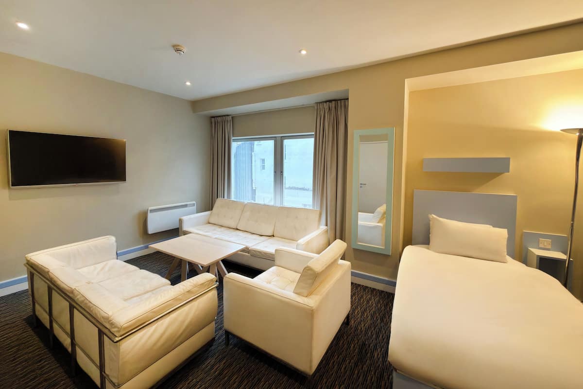 A hotel room with a sofa, two armchairs, a bed, a flat-screen TV, a mirror, and a window with curtains.