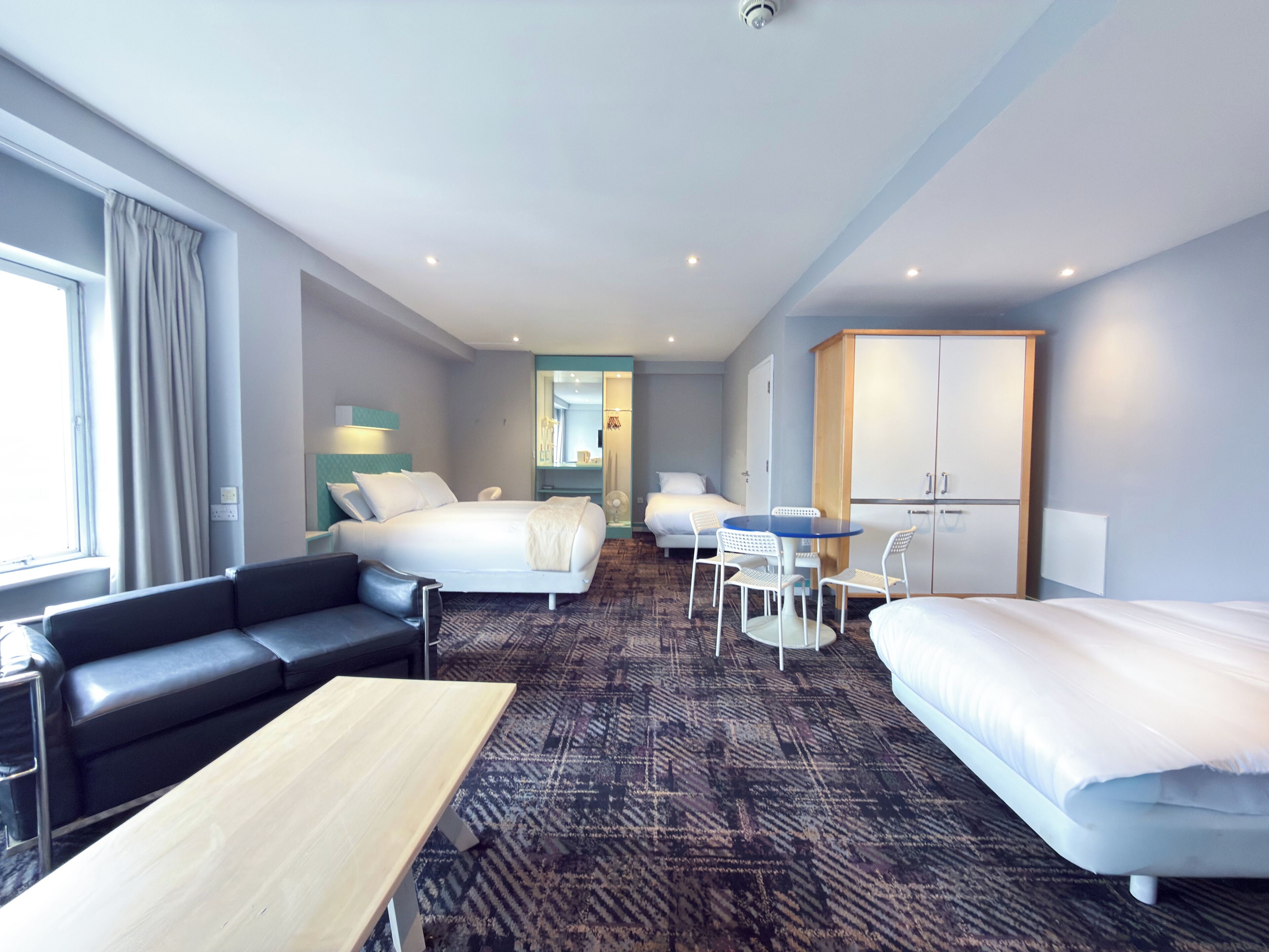 A hotel room with a bed, a sofa, a table, a desk, a wardrobe, and a mirror.