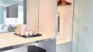 A modern hotel room with a large mirror, a minibar, a small refrigerator, and a clothing rack. - Citrus Hotel Cheltenham by Compass Hospitality (Cheltenham)