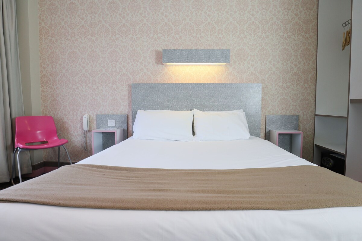 A hotel room with a bed, a nightstand, a telephone, a chair, and a wardrobe.