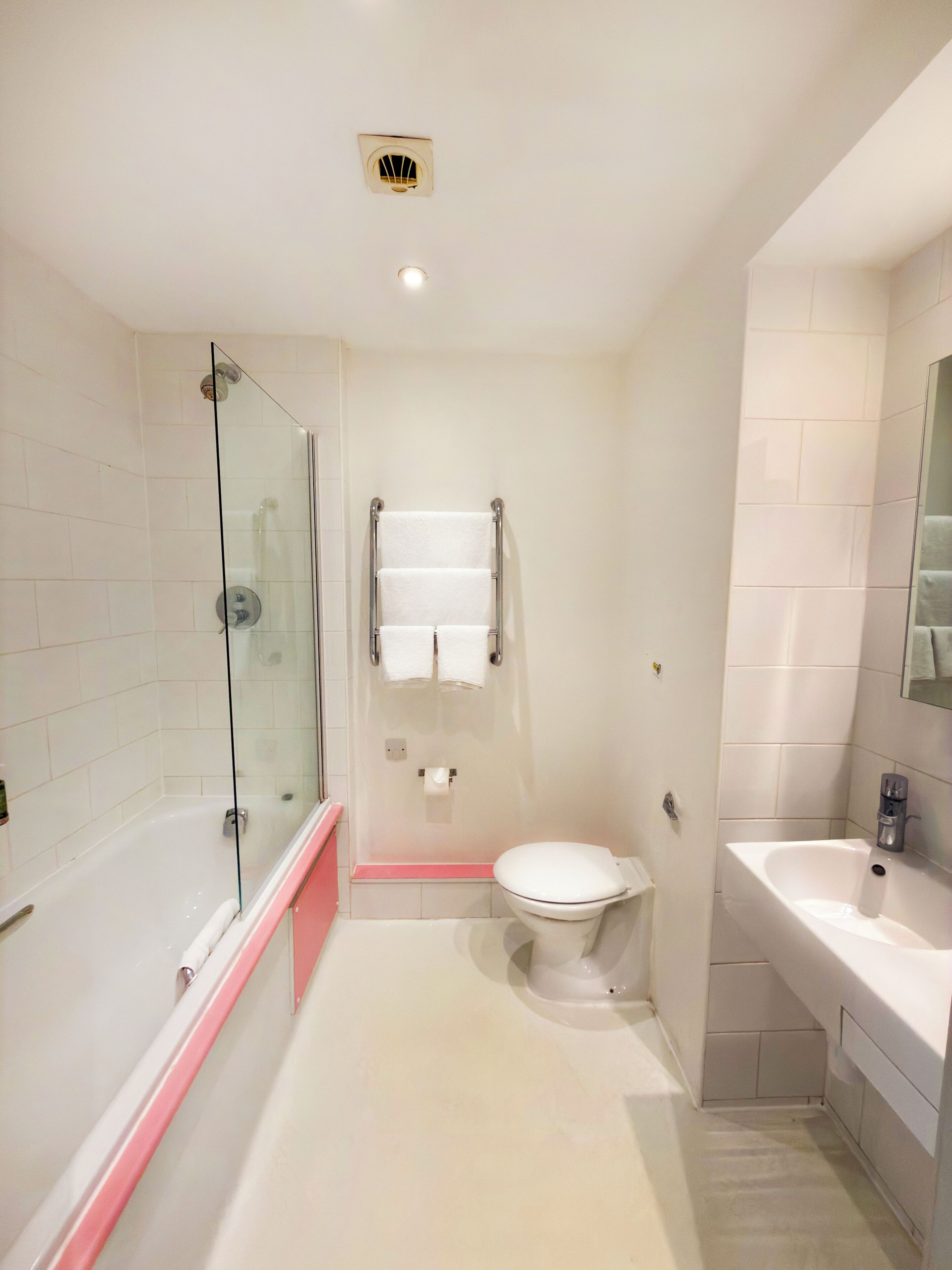 Une salle de bain avec une douche à parois de verre, des toilettes blanches, un lavabo et un porte-serviettes.