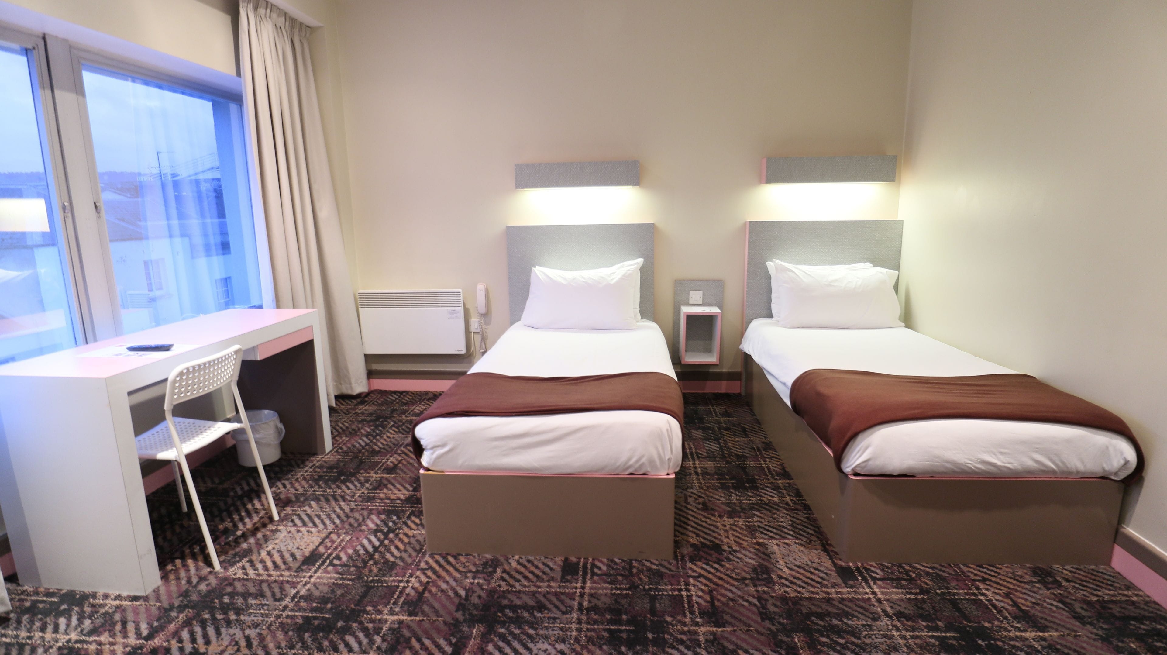 A hotel room with two beds, a desk, and a chair.