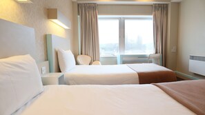 Habitación de hotel con dos camas, una ventana con cortinas, una silla y un calentador fijado a la pared.