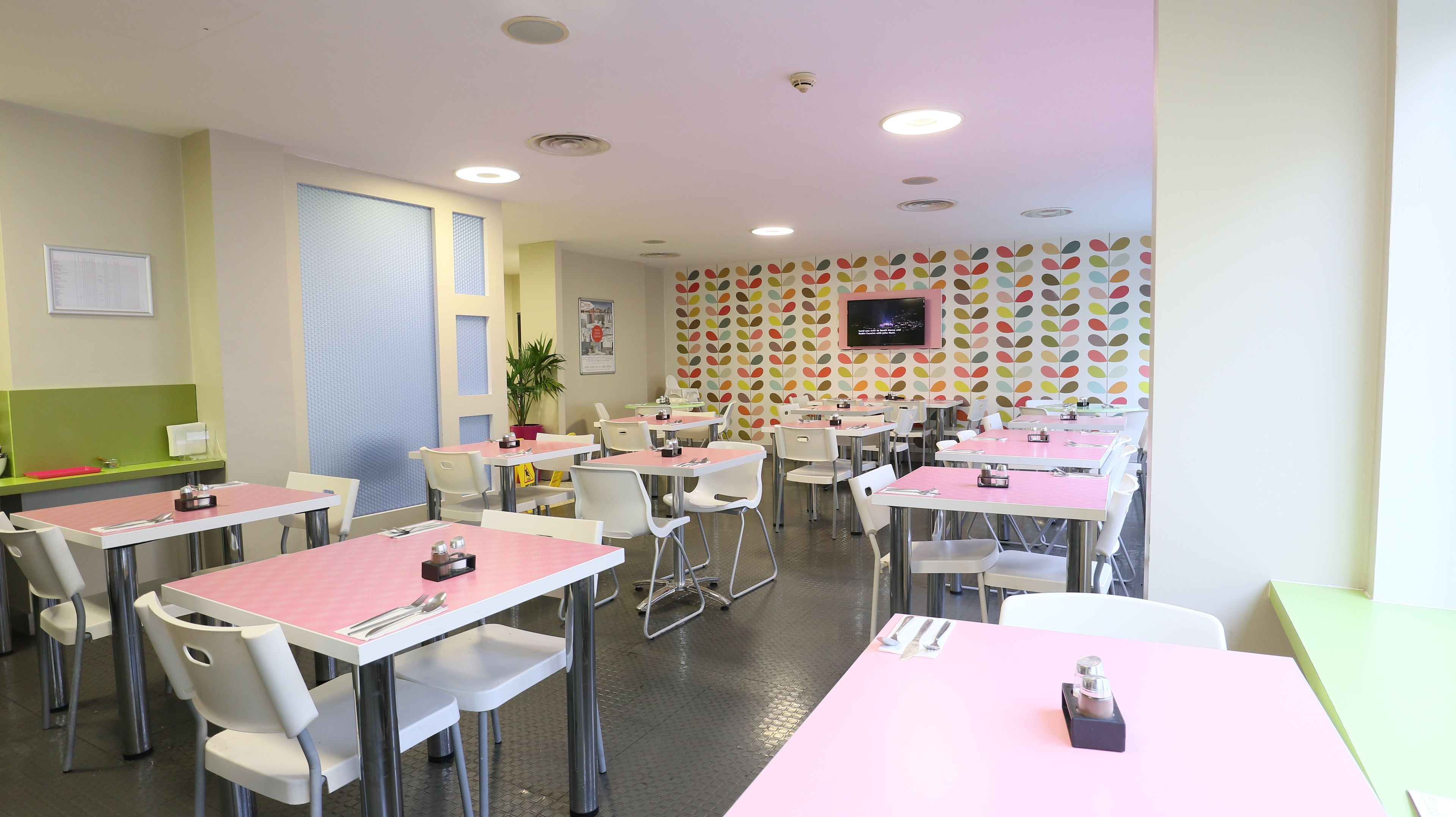 A dining area with tables and chairs, a television on the wall, and a patterned wall.