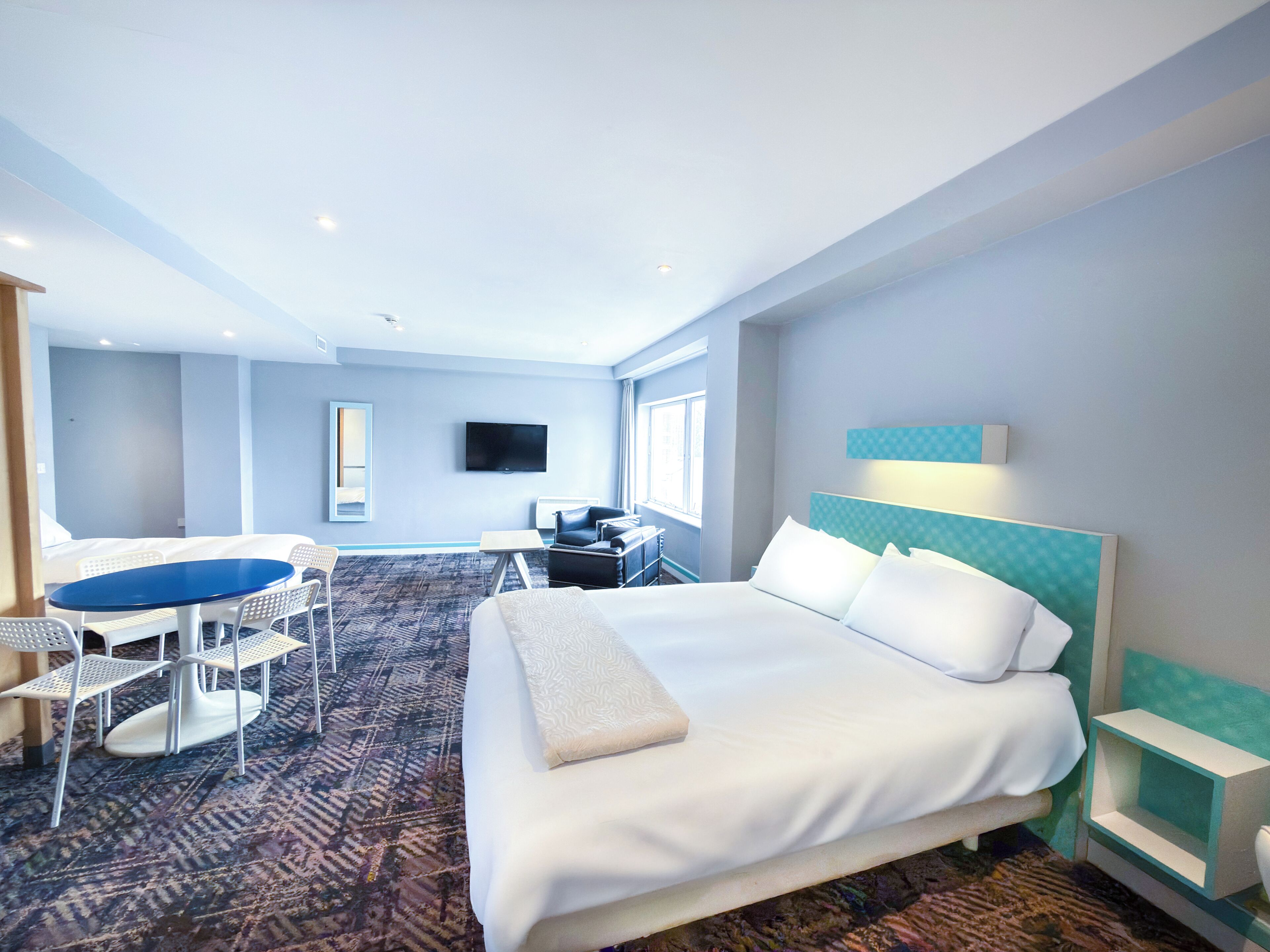 A hotel room with a large bed, a desk with a chair, a TV mounted on the wall, and a window.