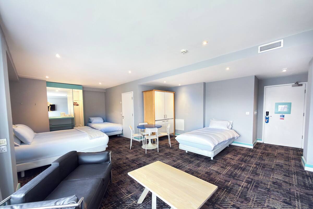 A hotel room with two beds, a sofa, a small table, a mirror, and a wardrobe.