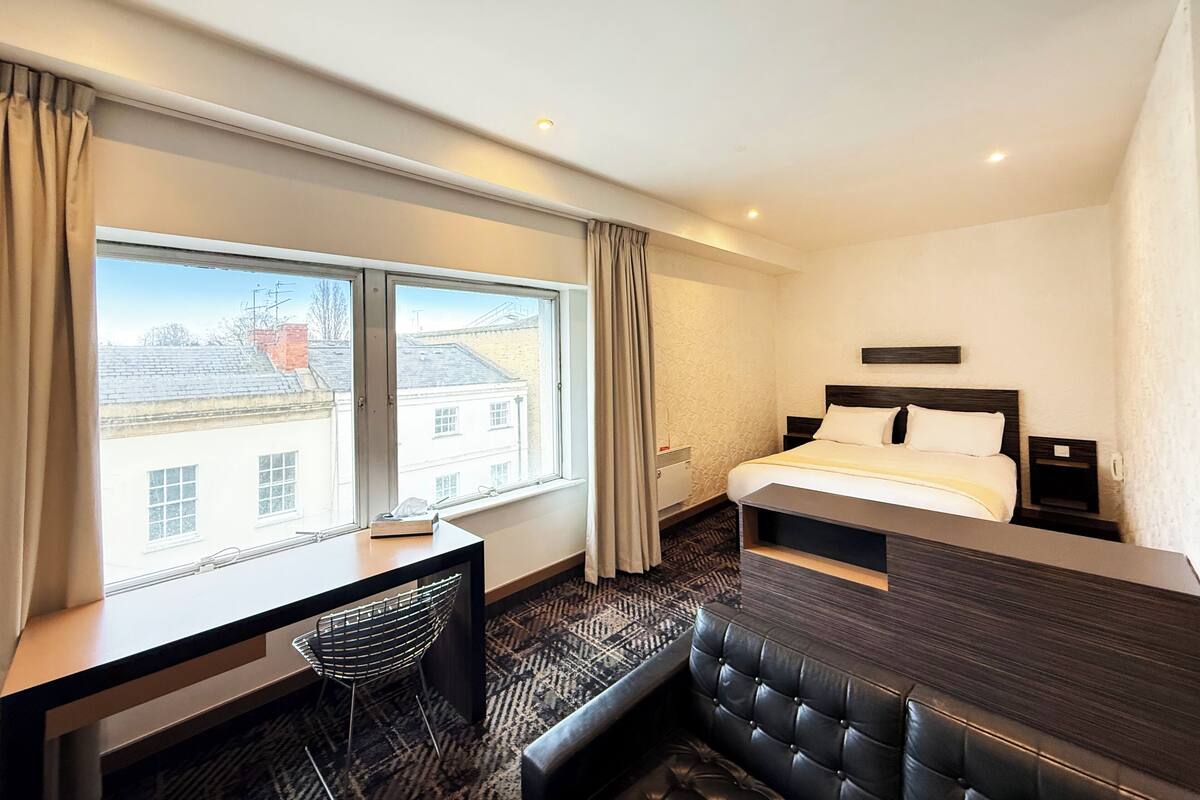 A hotel room with a bed, a desk, a chair, and a large window.
