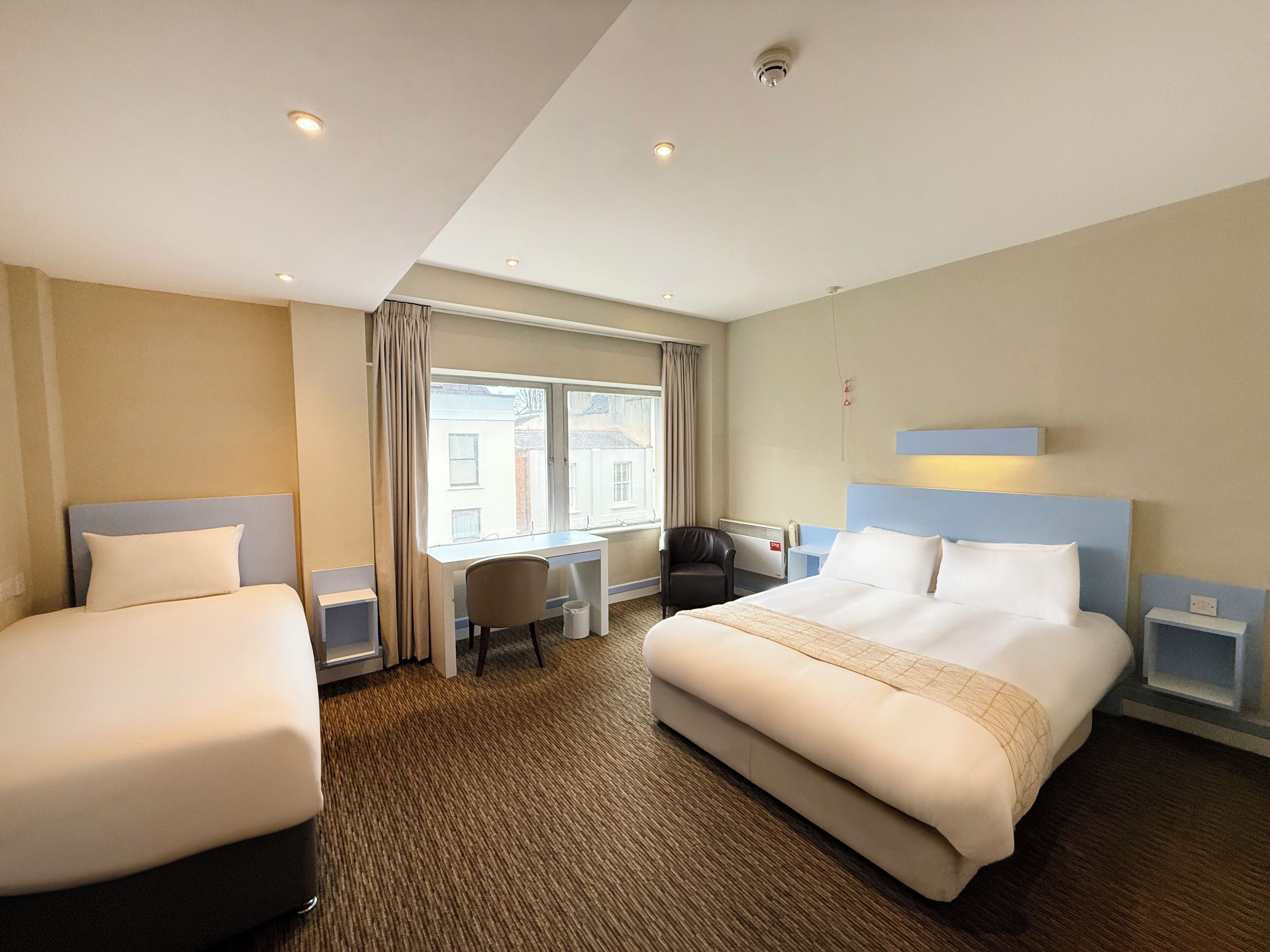 A hotel room with two beds, a desk, a chair, and a window.